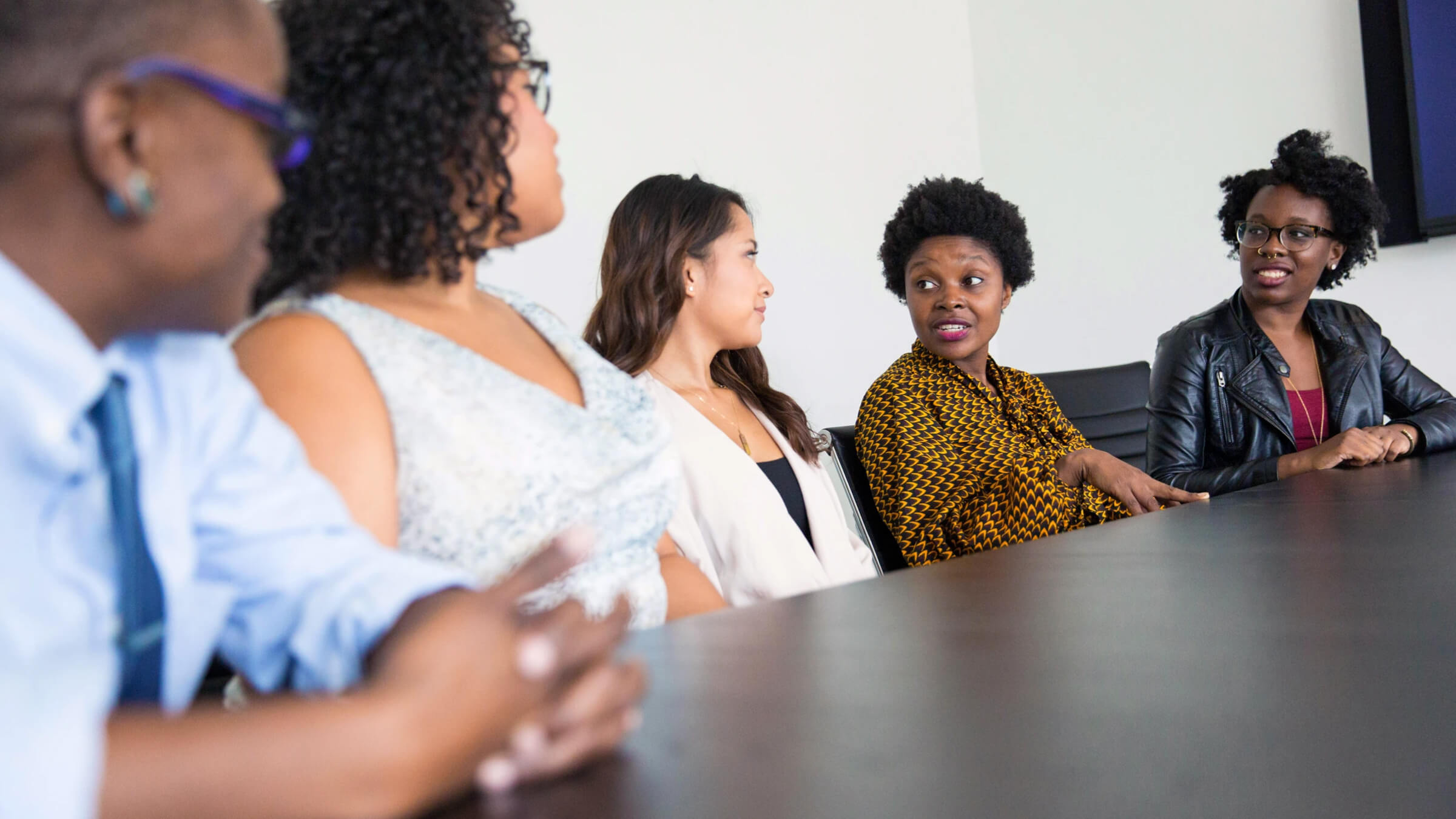 A diverse group of five professionals sitting at a conference table, engaged in a collaborative discussion in a bright office.