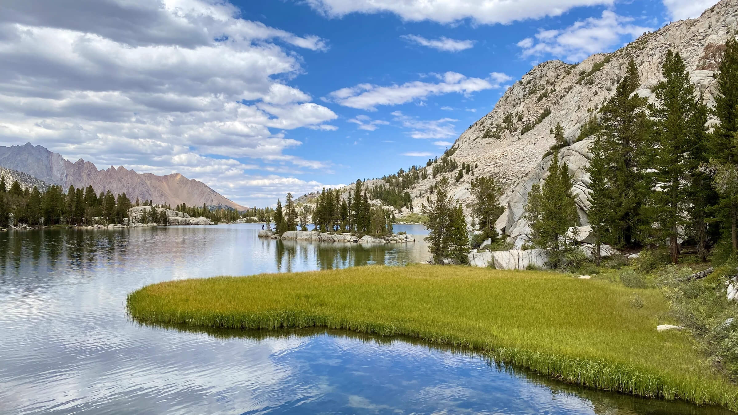 Alpine lake with granite mountains and trees under a partly cloudy sky