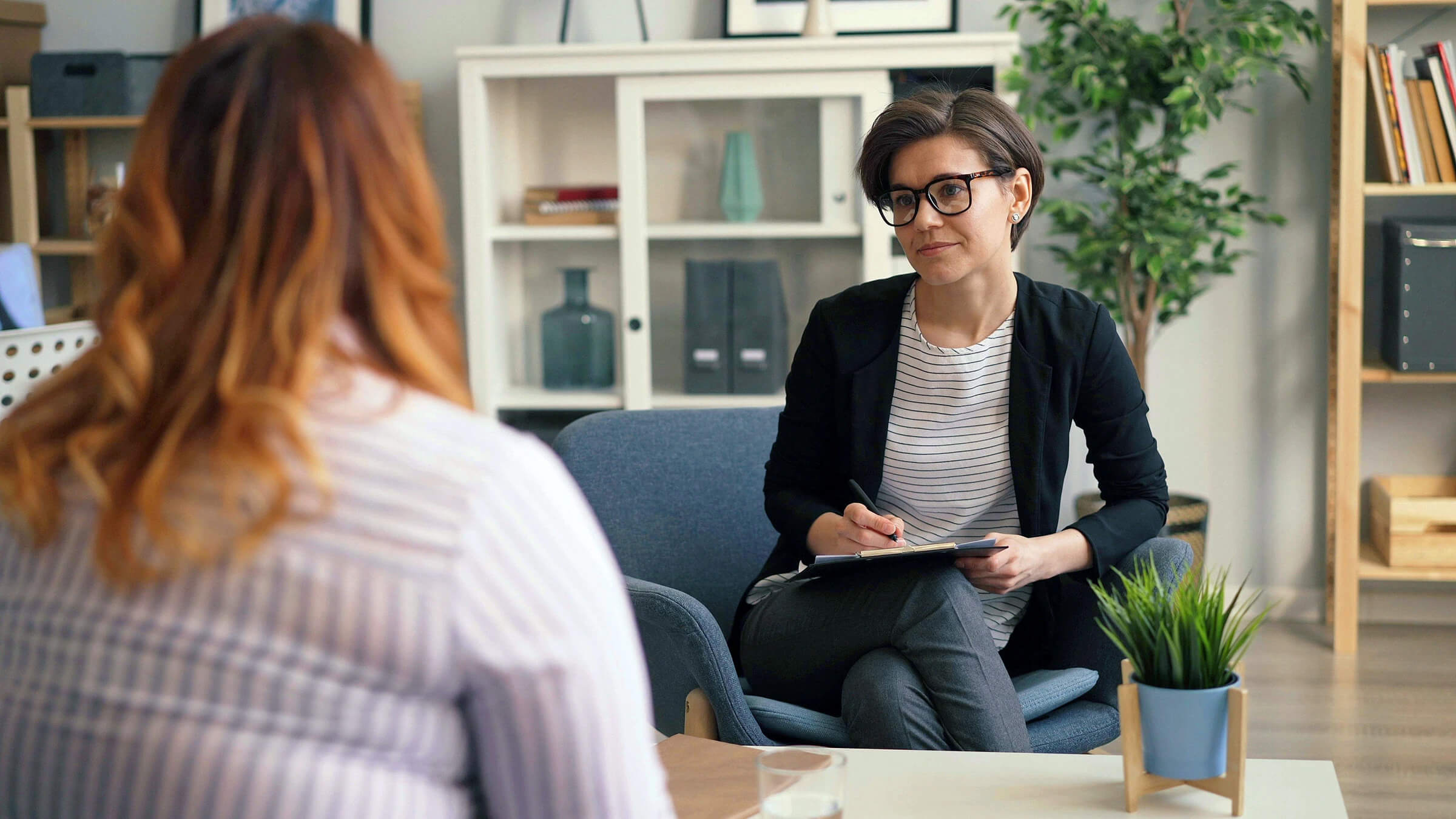 clinician seated in a chair taking notes while speaking with a patient in a calm office setting