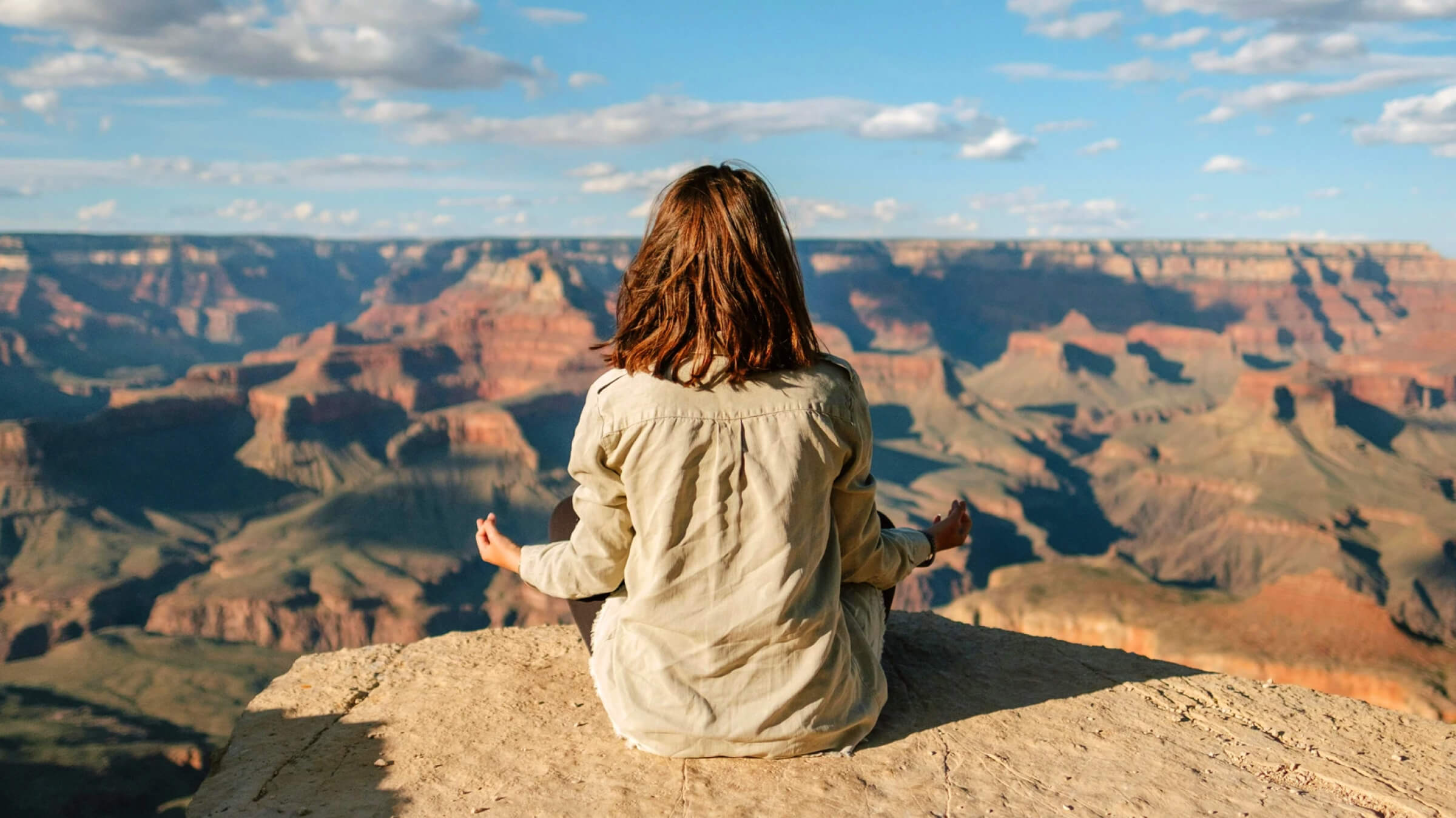 Person sitting cross-legged on a cliff overlooking a canyon, meditating with hands resting on knees