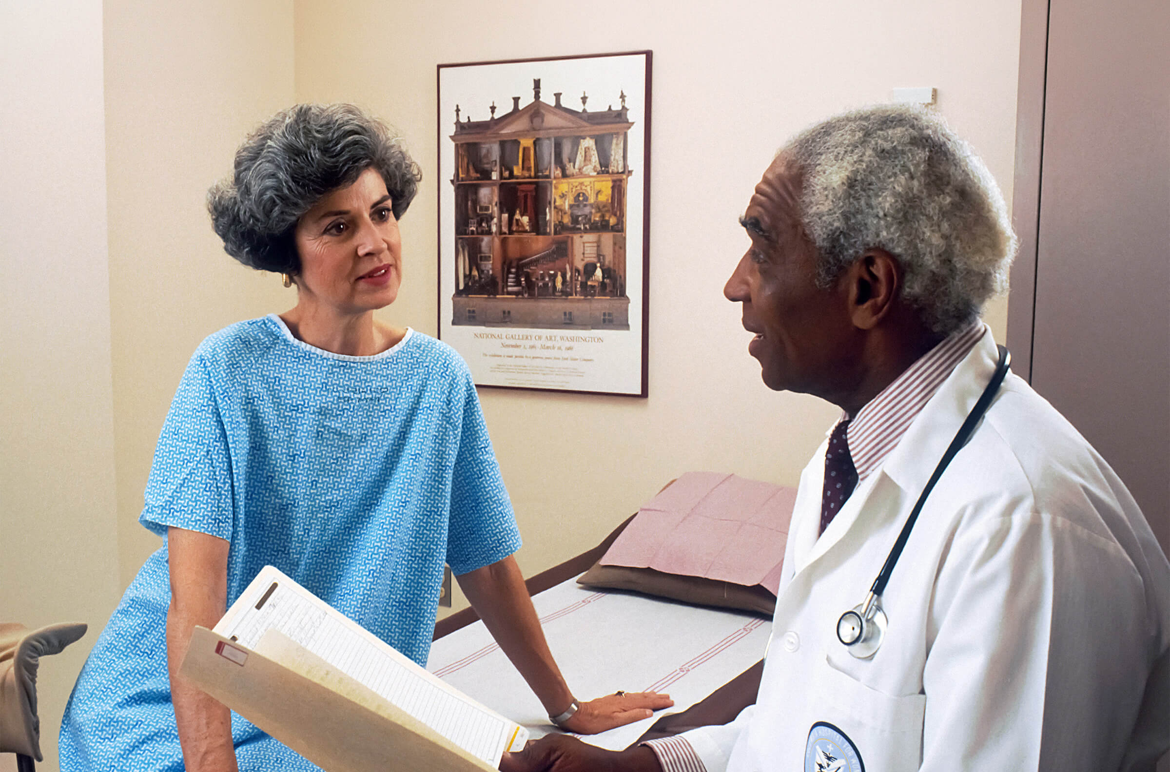  Doctor reviewing chart while speaking with patient in exam room