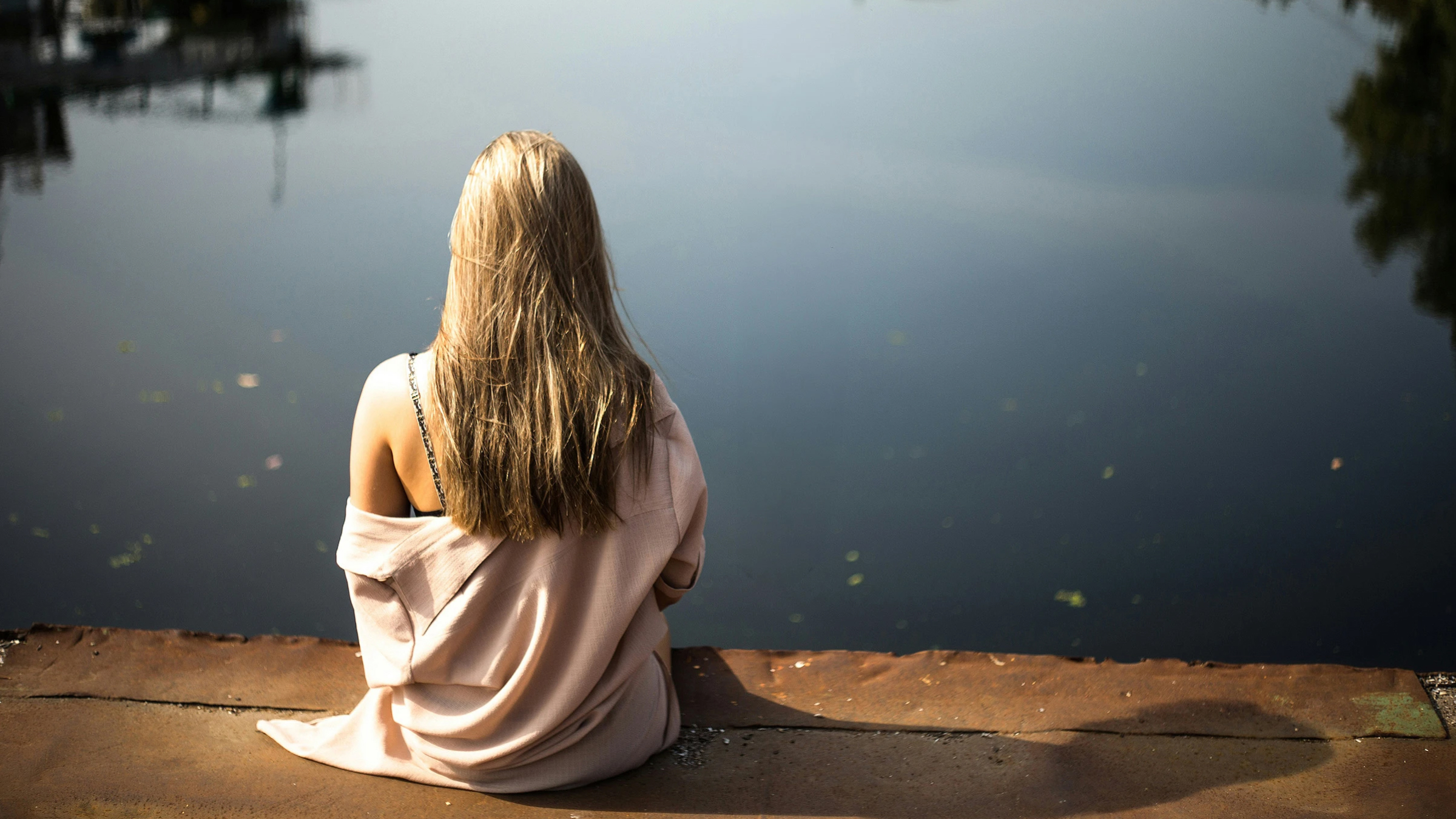 Person sitting by the water, viewed from behind.