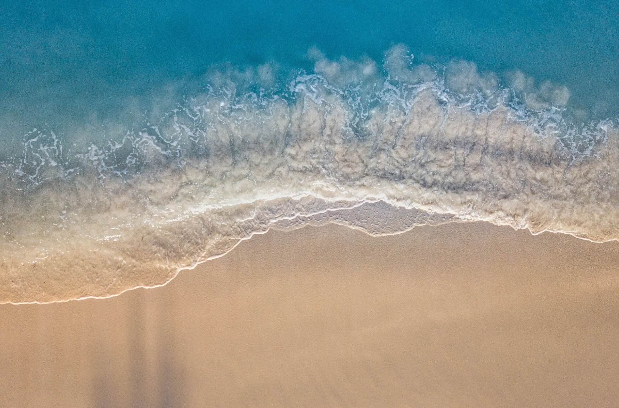 Aerial view of an ocean wave breaking onto a sandy beach.