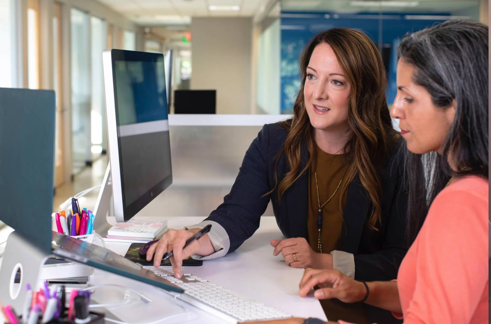 Two researchers collaborating at a computer in an office setting while reviewing research materials and planning a project.
