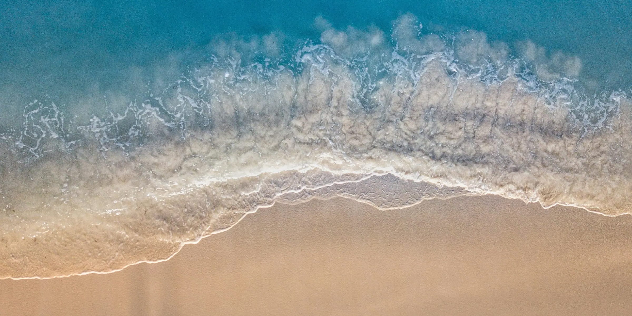 Aerial view of gentle ocean waves washing onto a sandy beach near San Diego, California. 