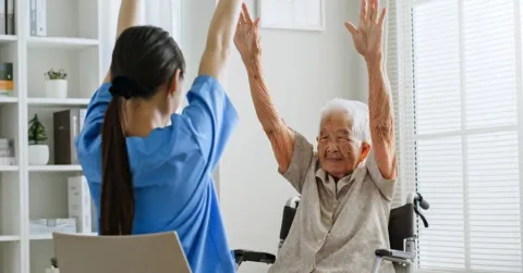 Young Asian woman nurse, caregiver assist a senior Asian woman to do physical therapy and exercise arms